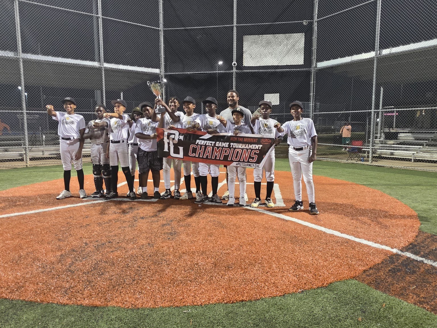 BBN Prospects players and coaches celebrating at night with a trophy and Perfect Game CHAMPIONS banner